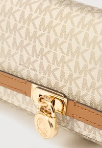 Portefeuille beige Michael Kors avec motif répété du logo MK, bordure en cuir marron clair, et serrure dorée ornée des initiales MK.