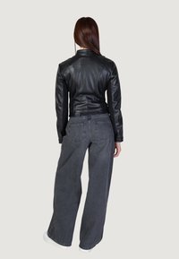 Svart läderjacka med figursydd överdel, ribbade axlar och långa ärmar, kombinerad med vida grå denimjeans och vita sneakers.