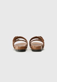 Brune lærsandaler med to justerbare stropper, flade såler og minimalistisk design. Glat tekstur, mat finish, ingen synlige mønstre.