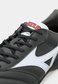 Adidași alb-negru cu o suprafață din piele netedă, accente contrastante, design cu șireturi și un logo distinctiv pe limba încălțămintei.