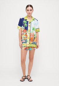 Set di camicia a maniche corte e pantaloni corti, realizzato in tessuto colorato con disegni di palme e edifici, con chiusura a bottoni e colletto a contrasto.
