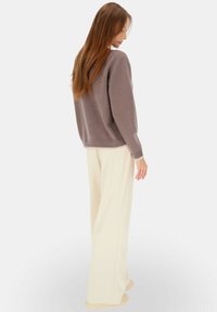 Szary sweter z prążkowanymi mankietami, zestawiony z luźnymi, kremowymi spodniami o szerokich nogawkach. Widoczna miękka faktura, zaprojektowany z myślą o komforcie i swobodzie ruchów.