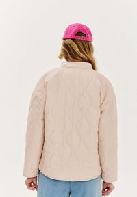 Prešívaná svetloružová bunda s textúrovaným vlnkovým vzorom, so vyvýšeným golierom a dlhými rukávmi, doplnená jasnoružovou čiapkou.