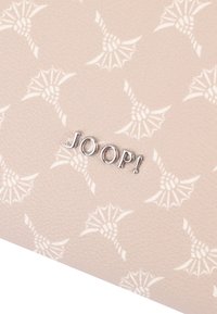 Portafoglio beige chiaro con motivo floreale in rilievo, caratterizzato da un logo metallico "JOOP!" ben visibile sul davanti. Superficie testurizzata.