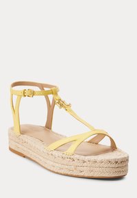 Žlutá kožená sandálová obuv se T-páskem a zlatou sponou a logem, s pletenou espadrilovou platformou.