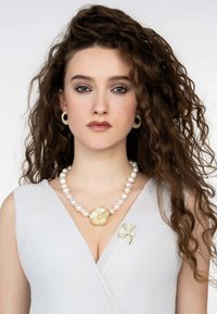 Pearl necklace with a gold floral pendant; matching gold and pearl brooch; model wearing a light gray, pleated dress.