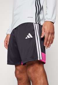 Svarte sportshorts med rosa detaljer, med hvite striper og Adidas-logo. Laget av et lett, fukttransporterende materiale.