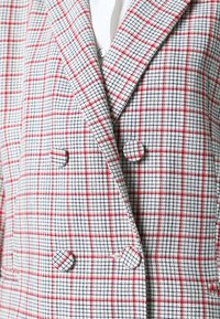 Dobbeltbrystet blazer med et rødt, sort og hvidt ternet mønster og stofbeklædte knapper over en hvid top.