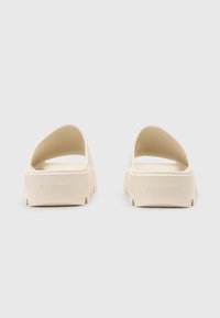 Beige rubber slide sandals with a smooth finish, open back, and low platform sole featuring subtle branding on the heel.