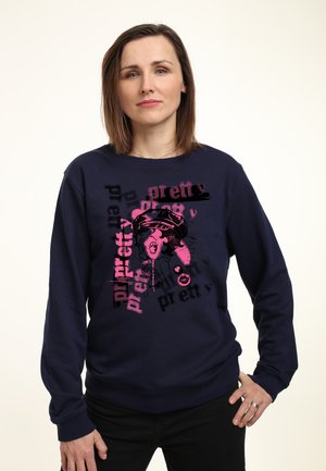 Marineblå sweatshirt lavet af blødt stof med et grafisk print, der viser en karakter og teksten "pretty" i pink. Ribbet kant og ærmer.