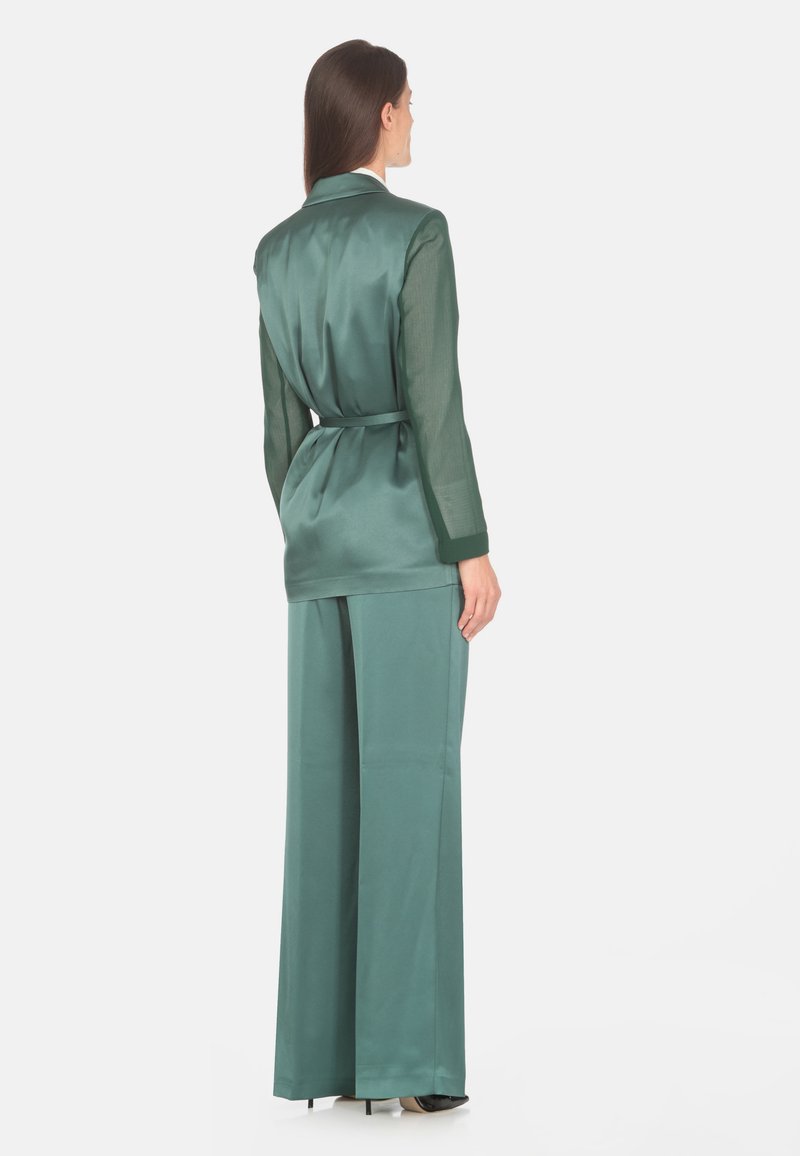 Costum din două piese din satin verde închis, care include o bluză cu mânecă lungă și talie încrucișată și pantaloni evazați, textură fină, design minimalist.