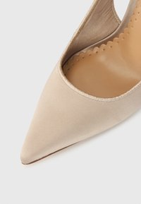 Μπεζ επίπεδο παπούτσι με μυτερή μύτη, πάνω μέρος από απαλό ύφασμα και εσωτερική επένδυση σε ανοιχτό καφέ χρώμα με ραφές σε σχήμα κυματιστού άκρου.