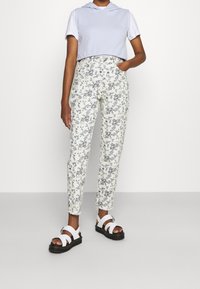 Haut à capuche bleu clair recadré, pantalon blanc à motifs floraux, et sandales noires avec des lanières blanches. Le pantalon est ajusté et possède des poches.