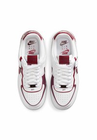 Białe sneakersy Nike Air Force 1 z bordowymi akcentami, perforowanym noskiem, płaskimi sznurowadłami oraz logo na języku i wkładce. Klasyczny design niskiego profilu.