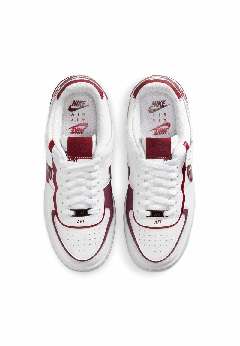 Hvide Nike Air Force 1 sneakers med burgunderfarvede detaljer, perforeret tå, flade snørebånd og branding på tungen og indersålen. Klassisk lavtop design.