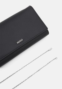 Zwarte leren portemonnee met een gevouwen ontwerp, voorzien van zilverkleurige hardware, een geperst "HUGO"-logo en een afneembare zilveren ketting.