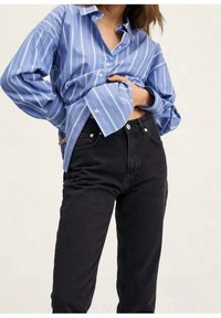 Camisa a rayas azul claro hecha de tejido entrelazado, con un corte relajado y cuello de botón, combinada con jeans negros de tiro alto.
