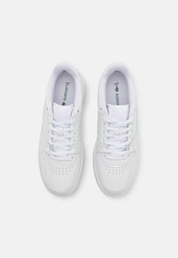 Valged nahast sneakersid perforatsioonide, lamede paelte ja tekstureeritud kummitaldaga. Sisetallas on roheline logo.