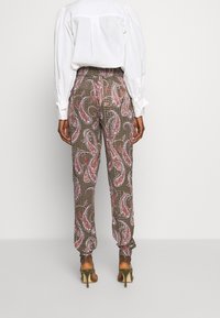 Pantalons à motif paisley multicolore en olive, avec une coupe ample et une taille élastique, associés à des talons hauts à lanières.