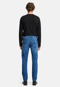 Jeans in denim blu con vestibilità dritta, tasche posteriori dettagliate e finitura testurizzata, abbinati a una maglia nera a maniche lunghe.