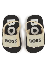 Crne japanke s debelim, teksturiranim potplatom; s bež trakama na kojima je ispisano "BOSS" crnim slovima preko prednje strane.