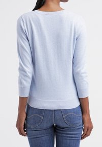 Ljusblå, stickad tröja med rund halsringning och trekvartslånga ärmar. Ribbad fåll och manschetter, slät textur. Bärs med blå jeans.