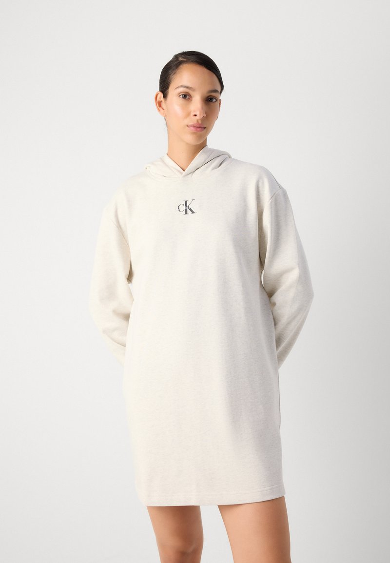 Hooded sweatshirt jurk in lichtbeige met een zachte textuur. Bevat een centraal logo, een losse pasvorm en lange mouwen, die eindigen boven het midden van de dij.