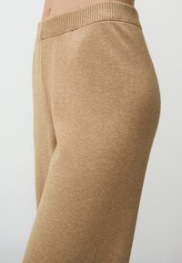 Joggings en mélange de coton beige avec une taille côtelée, présentant une texture lisse et une coupe effilée vue de côté.