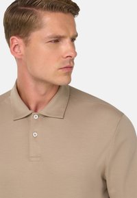 Polo beige realizzata in tessuto morbido, caratterizzata da un colletto, una chiusura a tre bottoni e discreti dettagli di cucitura.