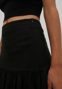Zwarte rok met een aangesloten taille en een uitlopende, geraffineerde onderkant. Inclusief een discrete zijrits. Glad materiaal met een zachte textuur.