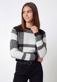 Sort og hvid ternet sweater med lange ærmer, ribbet manchetter og rund halsudskæring, båret over sorte bukser. Tekstureret strikstof.