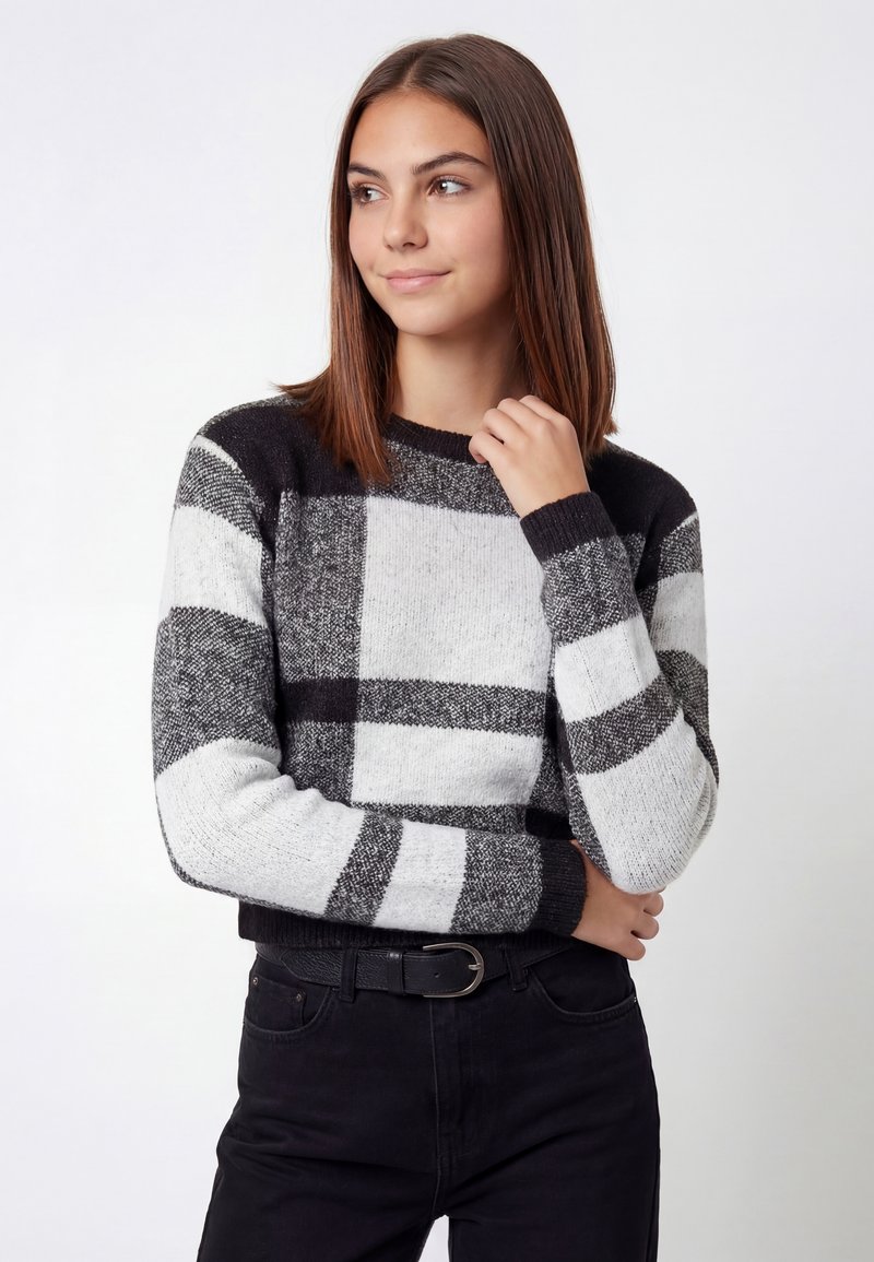 Sort og hvid ternet sweater med lange ærmer, ribbet manchetter og rund halsudskæring, båret over sorte bukser. Tekstureret strikstof.