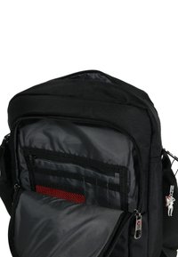 Zwarte stoffen boodschappentas met een ritssluiting van het hoofdvak, voorzien van interne zakken, een rode mesh-streep en een zilverkleurige metalen accent.