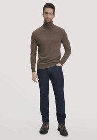 Brauner Rollkragenpullover, taillierte Passform, weicher Stoff, kombiniert mit dunkelblauen Jeans und braunen Schnürschuhen. Schlichte, klare Ästhetik.