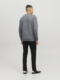 Grijze gespikkelde trui met lange mouwen, ronde hals en een relaxte pasvorm, gecombineerd met zwarte slim-fit broek en zwarte sneakers.