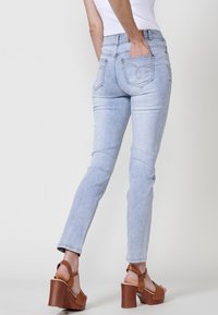 Vaqueros de denim azul claro con un diseño ajustado, cinco bolsillos y detalles de costura sutiles, combinados con sandalias de plataforma en tono beige.