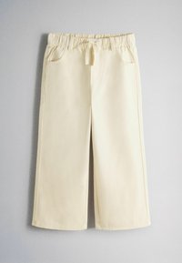 Pantalon crème à jambes larges avec taille élastique et cordon, poches avant, posé à plat sur une surface grise.
