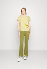 Top amarelo texturizado com mangas curtas, combinado com calças verdes caneladas com fendas laterais. Sapatos brancos chunky e uma pequena bolsa amarela.