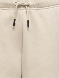Beige sweatpants med elastisk talje og justerbar snoretræk med sorte plastspidser. Blødt, glat stof med en fin tekstur.
