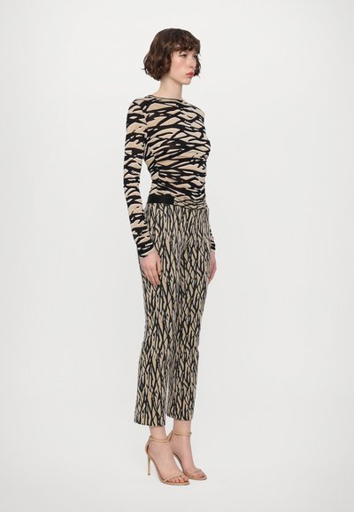 Long-sleeve top and patterned pants in beige and black, featuring abstract designs. Model wears strappy nude heels.