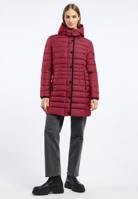Bordeaux puffer coat met een capuchon, horizontale quilt, zwarte accenten, knoopsluiting en zijzakken, gecombineerd met grijze broek en zwarte laarzen.