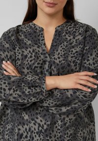 Zwarte en grijze blouse met een V-hals, lange mouwen en knoopaccenten op de manchetten. Zachte, gestructureerde stof met een abstract dierenprint.