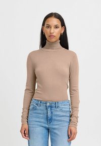 Maglione girocollo beige in tessuto a costine, design aderente, maniche lunghe. Abbinato a jeans azzurri chiari, con un classico stile a cinque tasche.