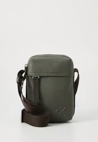 Green leather crossbody bag with a textured finish, brown adjustable strap, zip closure, and embossed logo on the front.