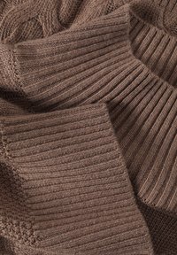 Braun gestrickter Stoff mit einer Mischung aus gerippten und strukturierten Mustern, bei dem verschiedene Stichstile Tiefe und Interesse erzeugen.