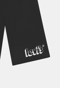 Černé bavlněné šortky s hladkou texturou a bílým potiskem loga "levi's" na spodní levé noze.