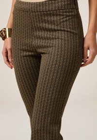 Leggings noir et doré avec un motif géométrique, présentant une texture lisse et un style ajusté. Accentués par une large ceinture.
