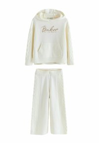 Balts adīgs divdaļīgs komplekts, kas ietver kapuci ar priekšējo kabatu un "Baker" tekstu, apvienojumā ar platām biksēm ar teksturētām detaļām.