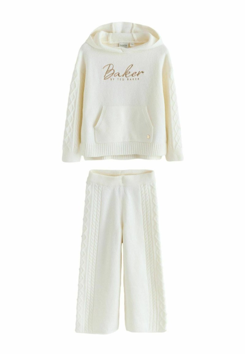 Balts adīgs divdaļīgs komplekts, kas ietver kapuci ar priekšējo kabatu un "Baker" tekstu, apvienojumā ar platām biksēm ar teksturētām detaļām.