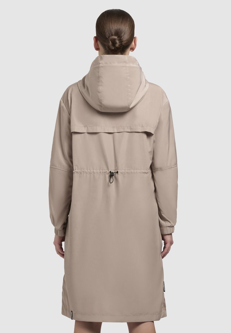 Manteau long beige avec capuche, poignets élastiques et taille ajustable à cordon. Matière lisse et légère avec un design simple et pratique.